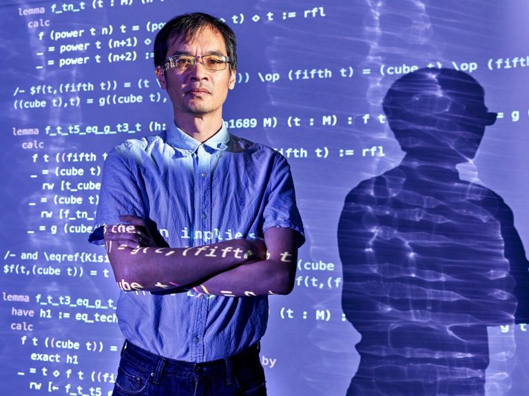 a-photo-shows-a-man-standing-in-front-of-the-projection-of-a-computer-screen-thats-filled-with-computer-code