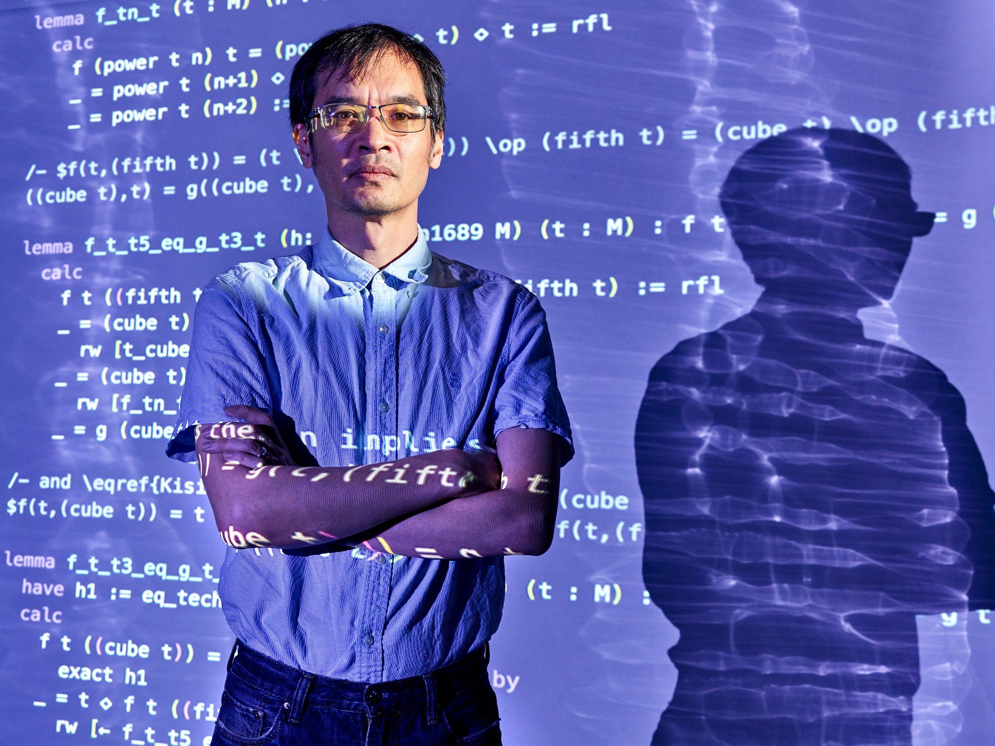 a-photo-shows-a-man-standing-in-front-of-the-projection-of-a-computer-screen-thats-filled-with-computer-code
