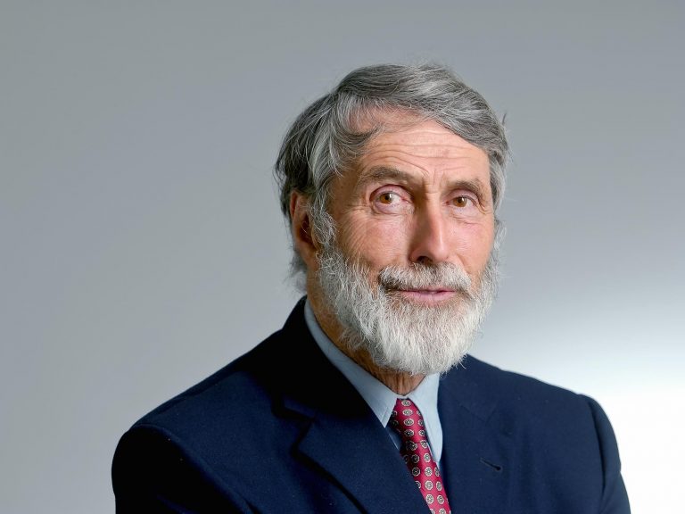 portrait-of-a-bearded-white-man-with-gray-hair-smiling-in-a-blue-suit-with-red-tie
